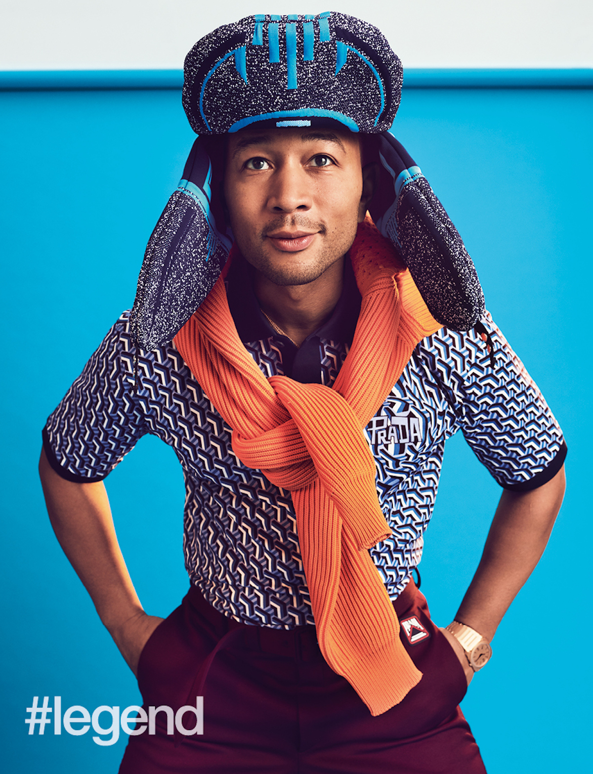 Octo Finissimo Automatic Sandblasted 40mm watch in sandblasted 18k pink gold by Bulgari; blue trapper hat, orange sweater, blue printed polo, and burgundy trousers by Prada