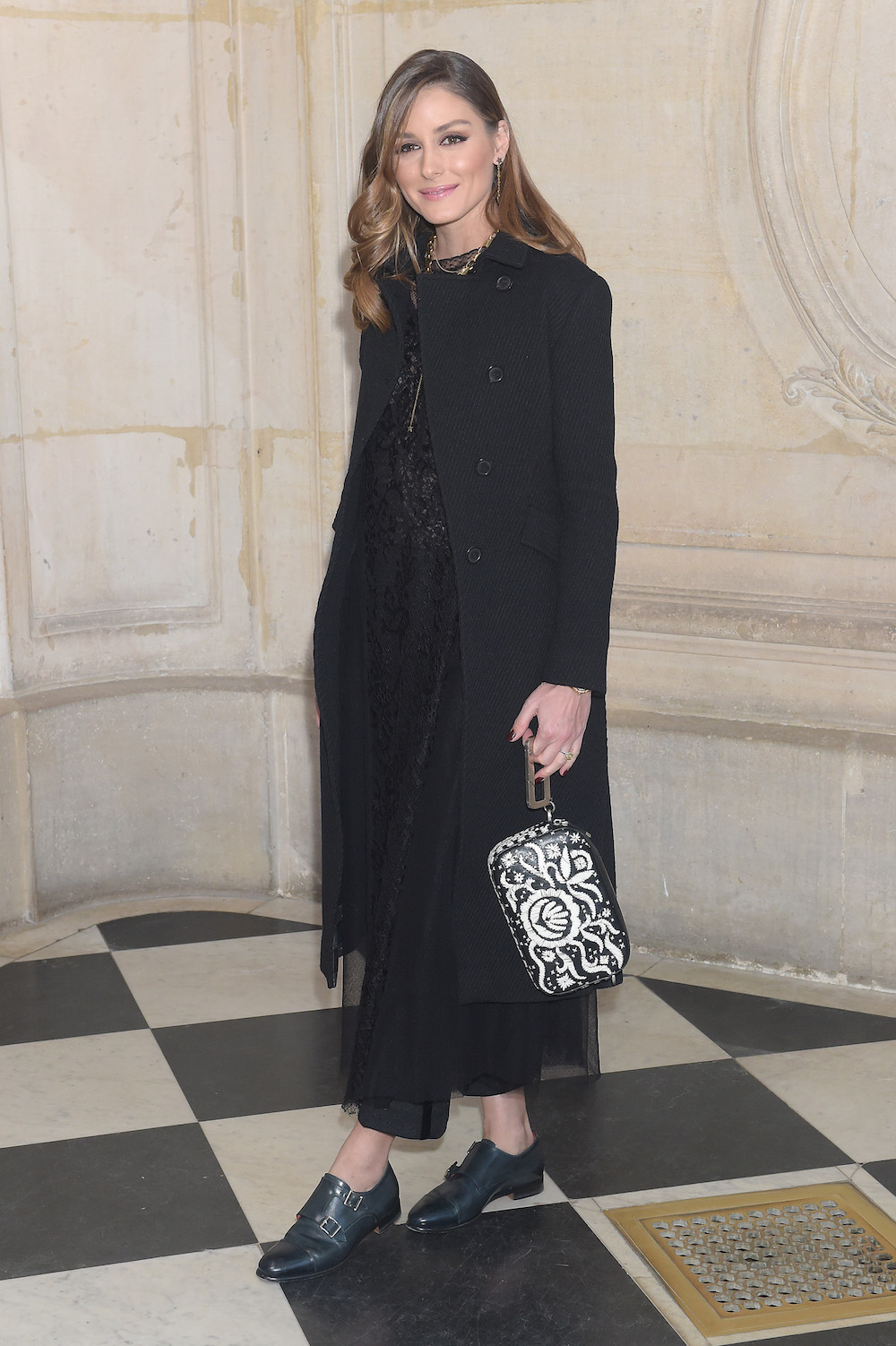 Olivia Palermo in Dior Fall 2019 black wool coat, a Dior Fall 2019 black lace dress, a Diorquake black printed leather clutch and Dior shoes.