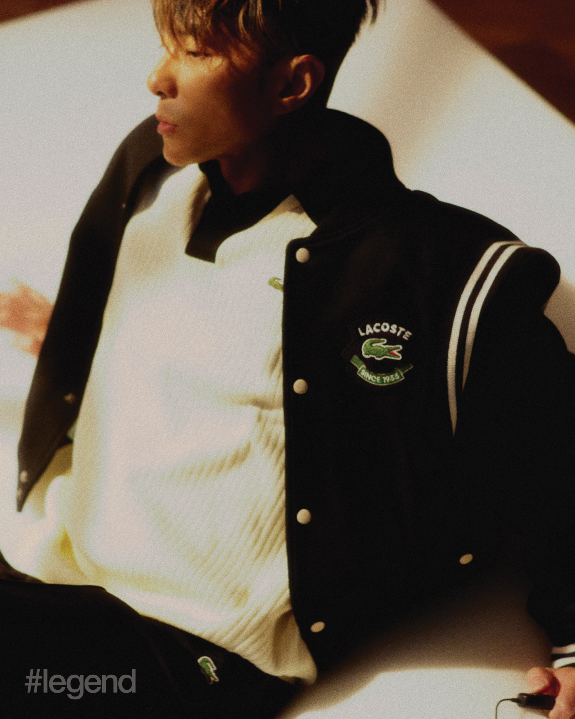 Varsity jacket, beige polo sweater, black sweatpants _ Lacoste